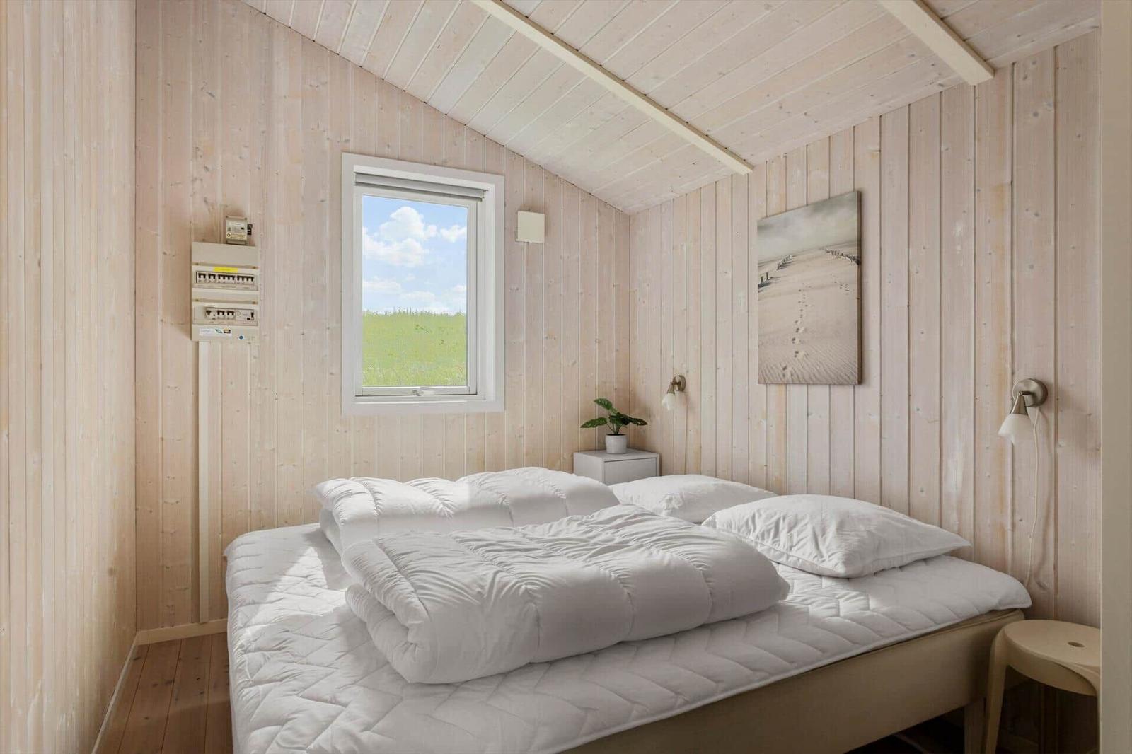Schlafzimmer mit Holzwand, Bett und Fenster mit Blick auf Gras.