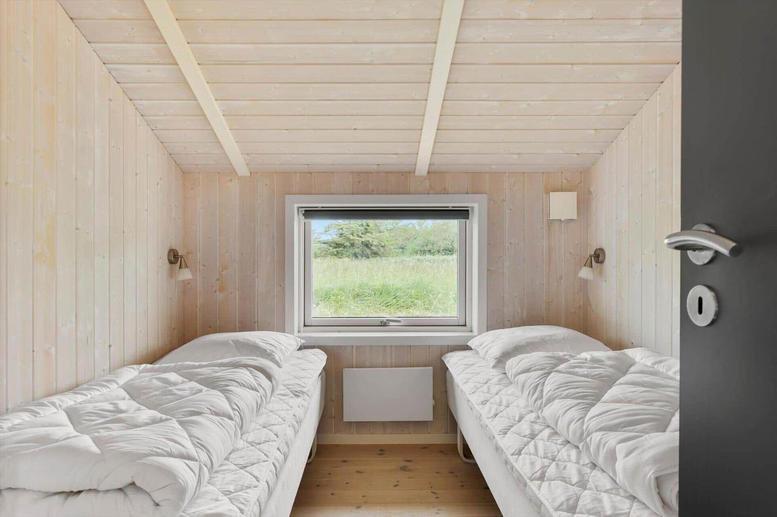 Zwei Betten in einem holzverkleideten Raum mit Fenster und Heizung.