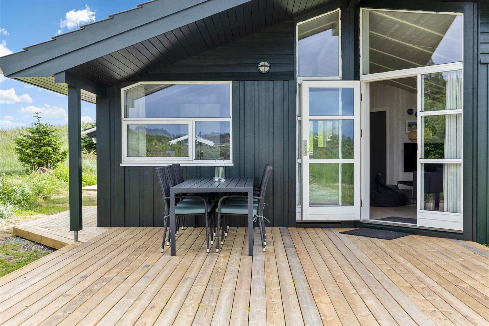 Terrasse mit Tisch und Stühlen vor einem Haus mit Glasfront.