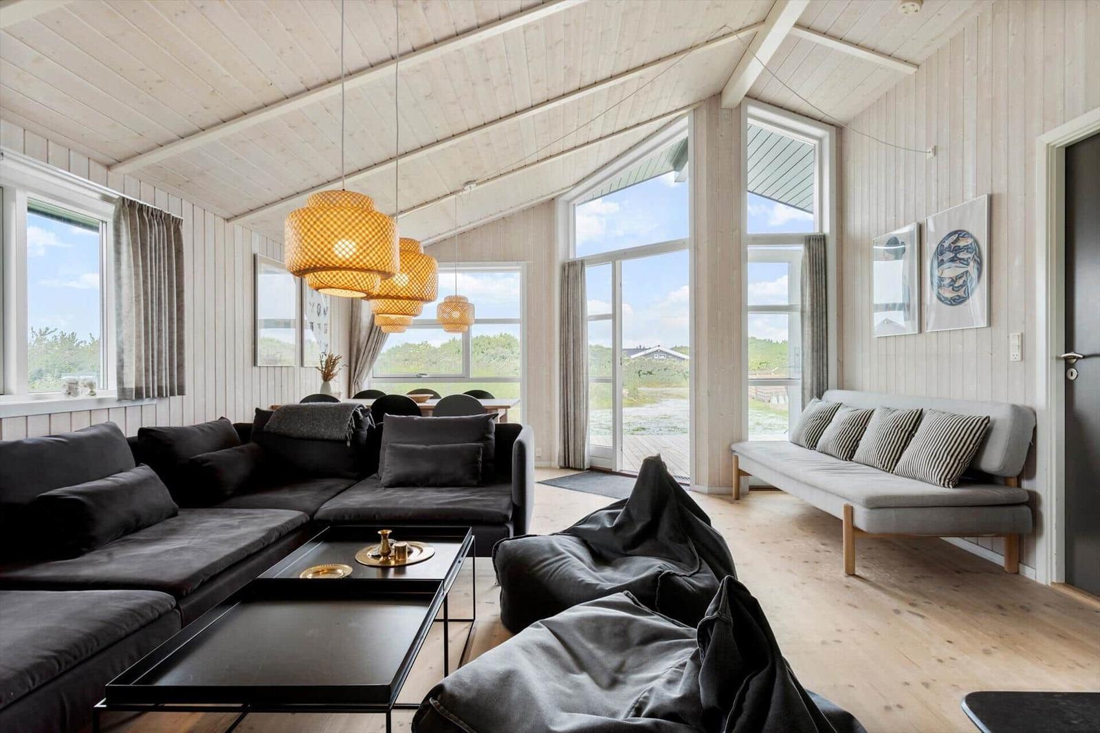 Wohnzimmer mit Sofa, Couchtisch und großen Fenstern. Holzdecke und -wände.