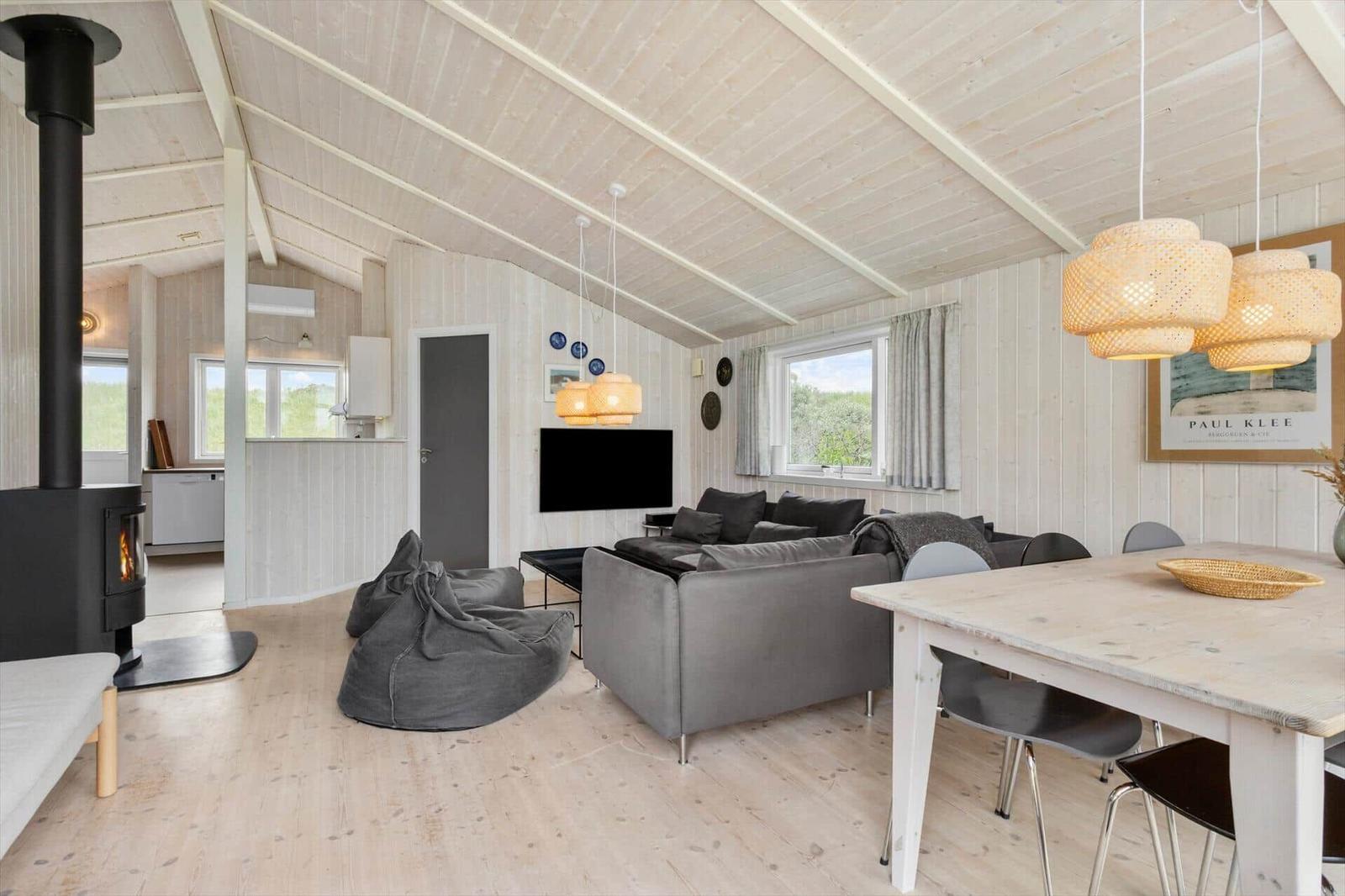 Wohn- und Essbereich mit Sofa, Esstisch und Kaminofen. Holzwände und Decke.