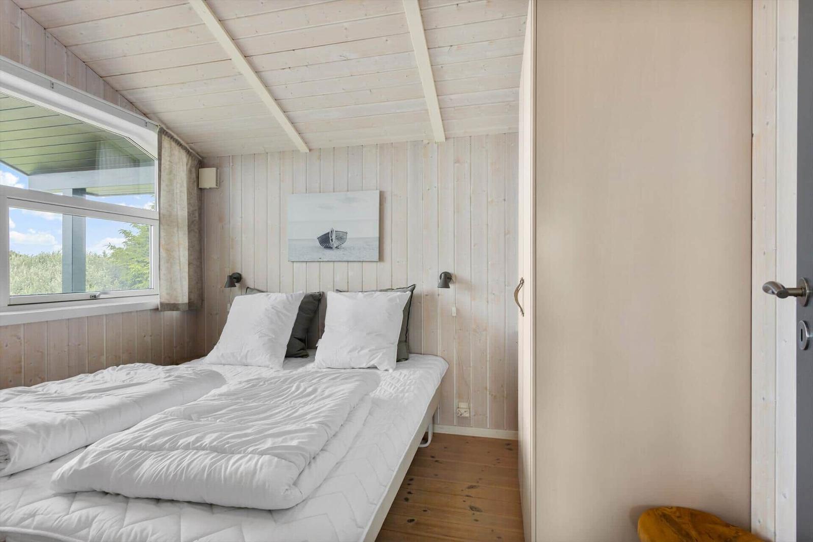 Schlafzimmer mit Bett, Fenster und Holzwand. Wandbild und Schrank sind sichtbar.