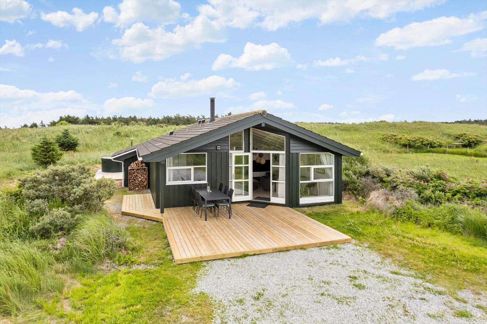 Moderne Holzhütte mit Terrasse und Garten. Große Fenster, Grill und Holzstapel.