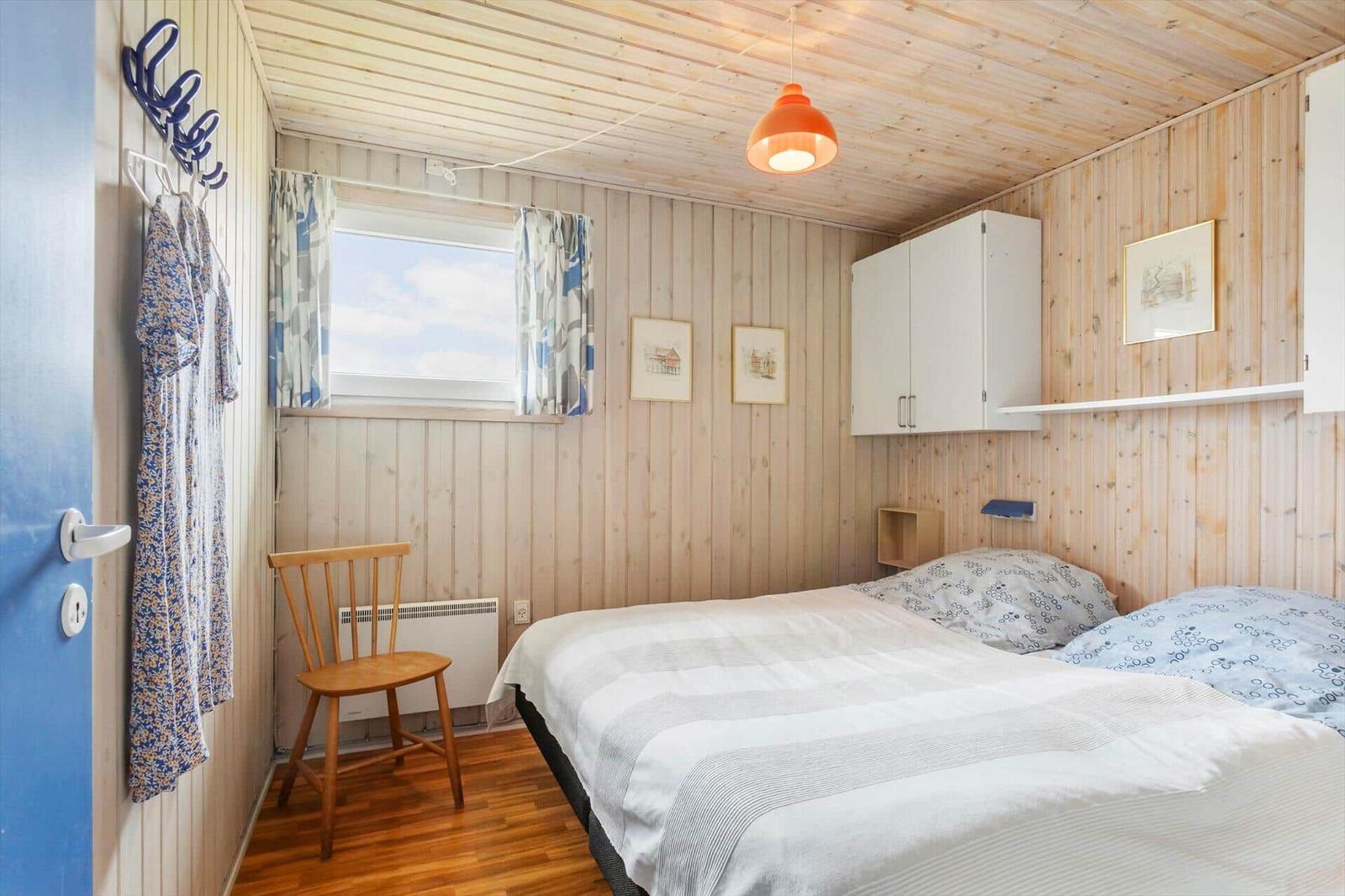 Ein Schlafzimmer mit Holzwänden, einem Bett, einem Stuhl und einem Fenster.