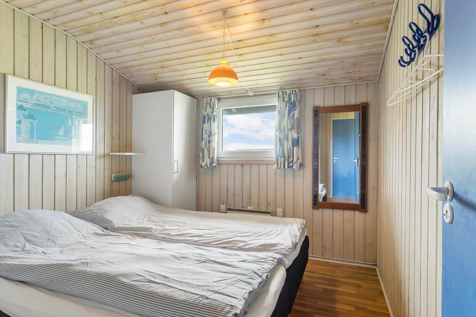 Schlafzimmer mit Holzwand, Bett, Fenster und Spiegel.