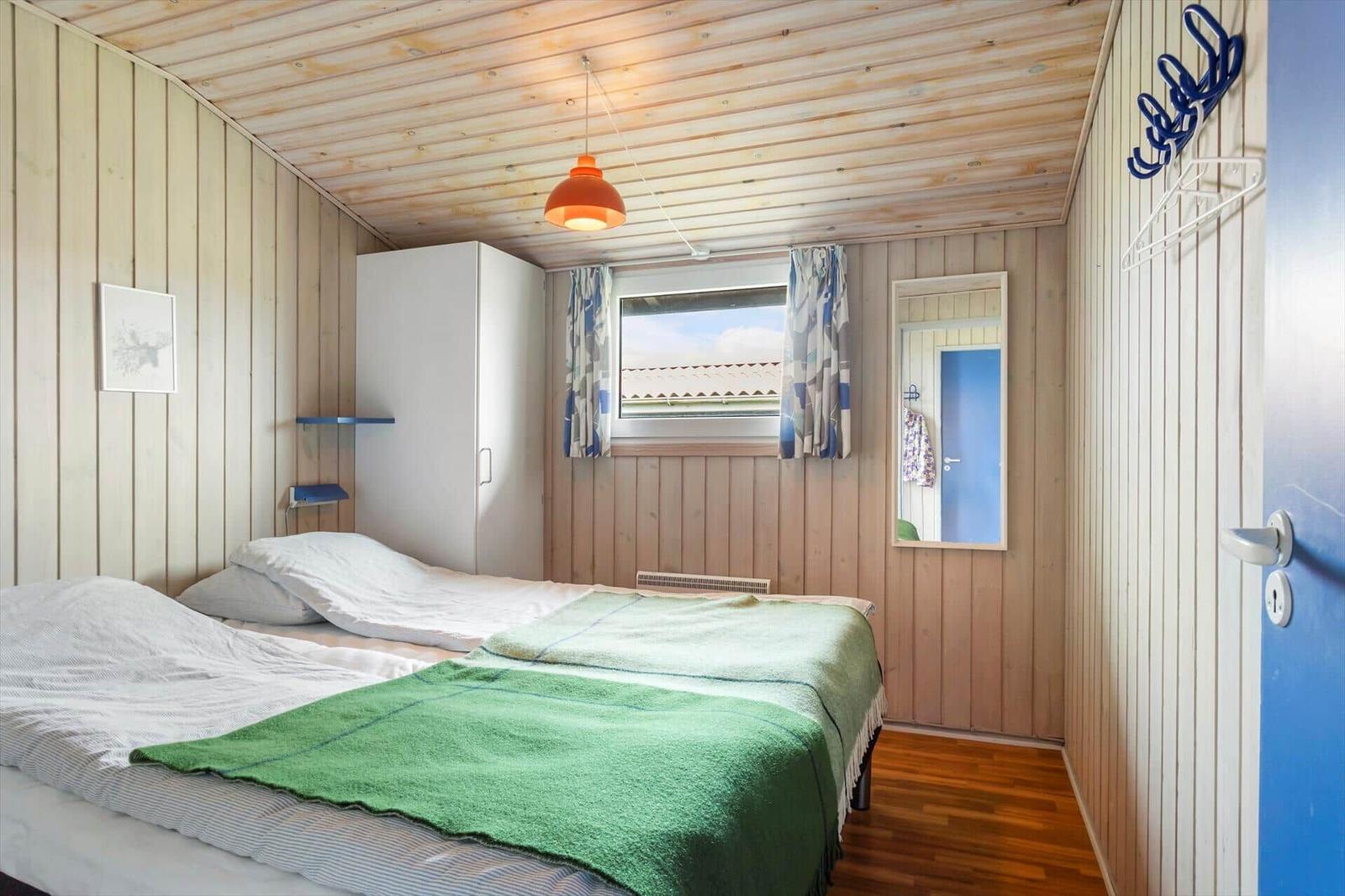 Schlafzimmer mit Bett, Kleiderständer und Fenster. Holzwand und Decke.