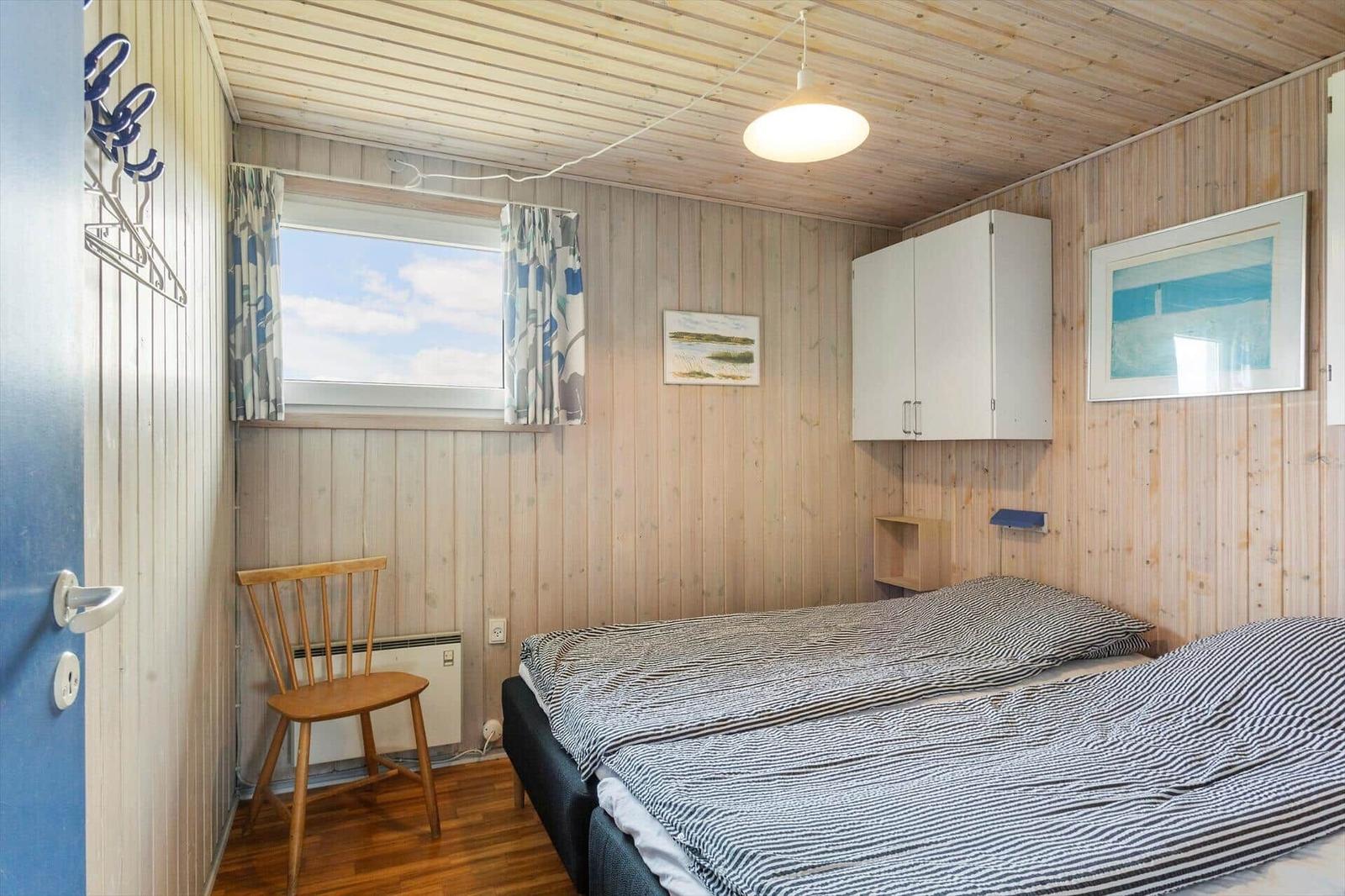 Schlafzimmer mit Holzwand, Bett, Stuhl und Fenster mit Vorhängen.