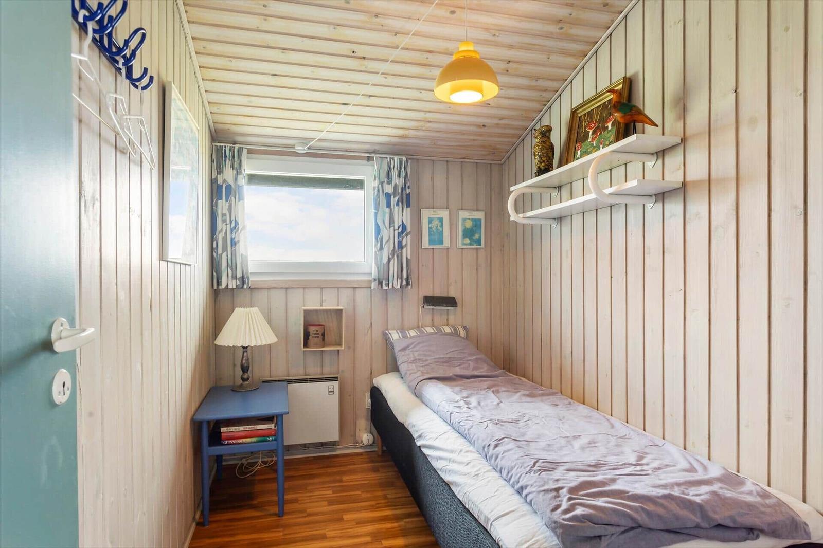 Schlafzimmer mit Bett, Nachttisch und Fenster mit Vorhängen.