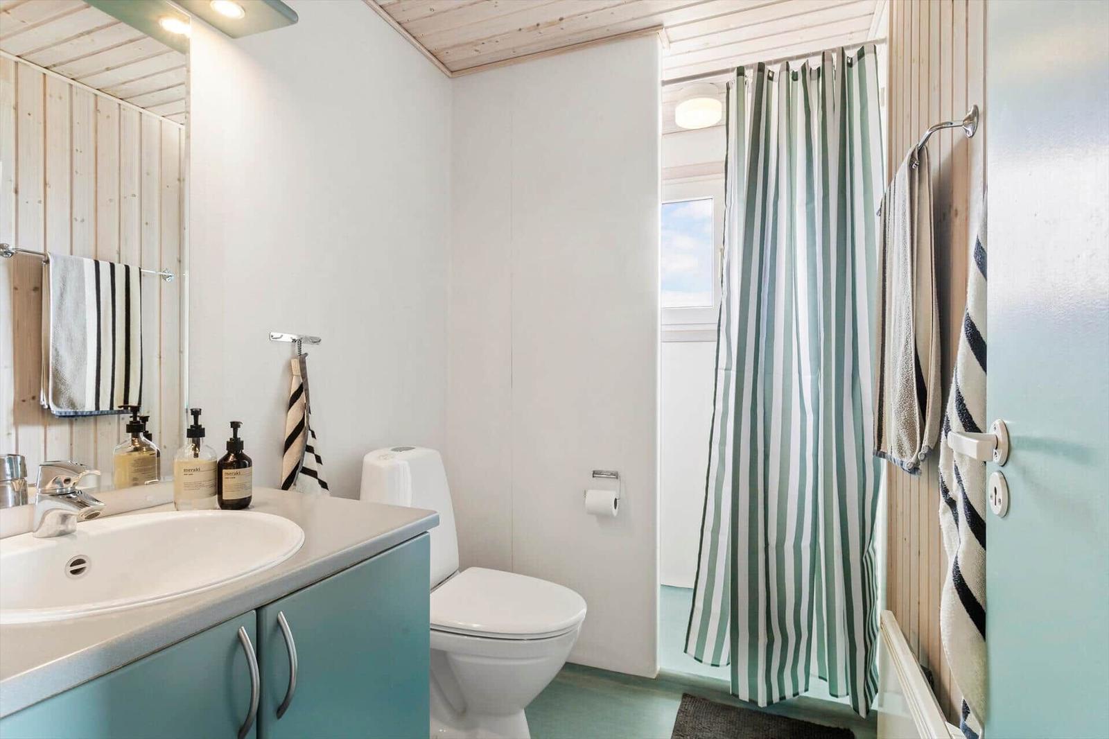 Badezimmer mit Waschbecken, Toilette und Dusche mit Streifenvorhang.