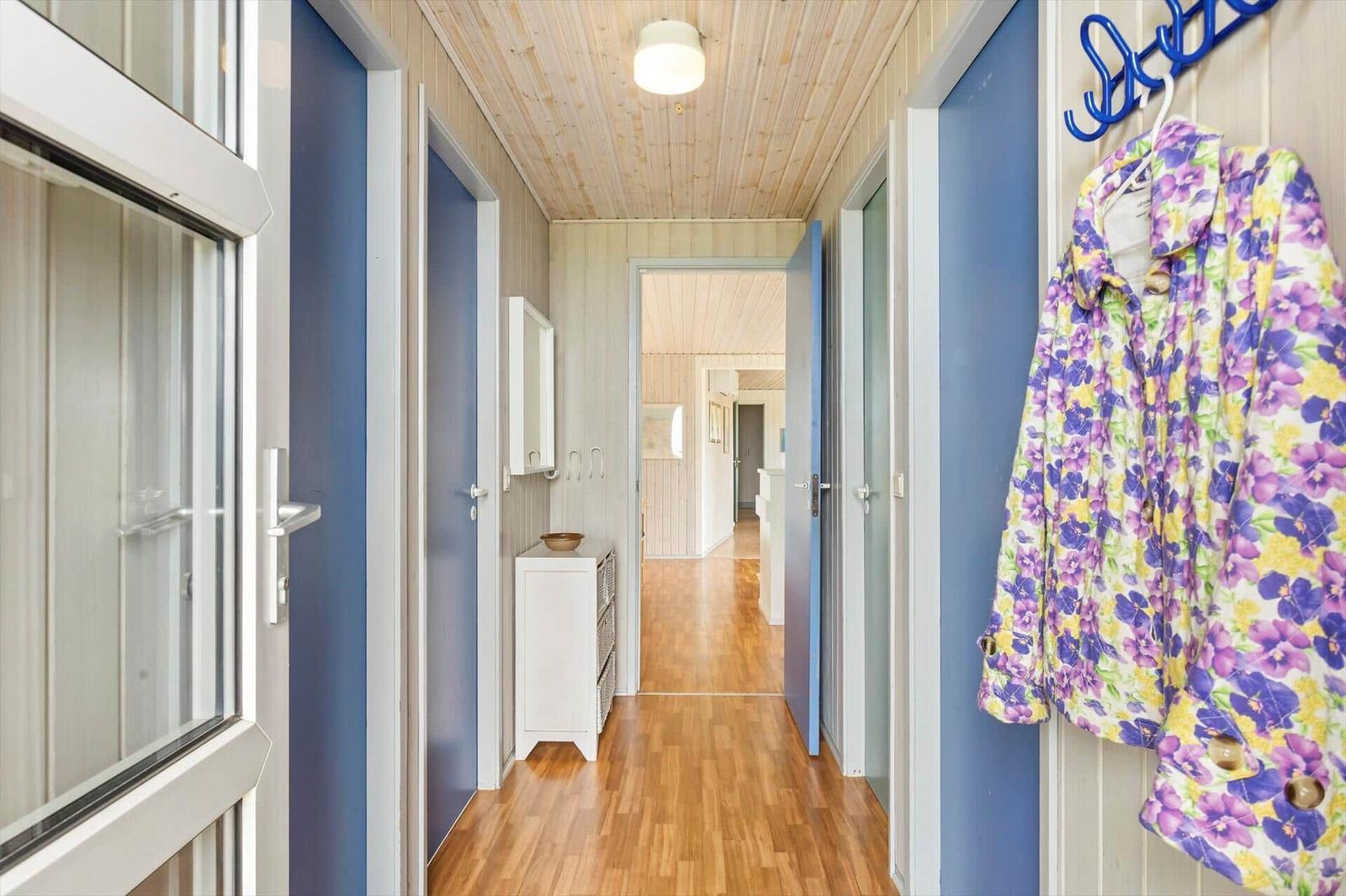 Flur mit Holzboden, blauen Türen und einem weißen Schrank. Eine Jacke hängt an einem Haken.