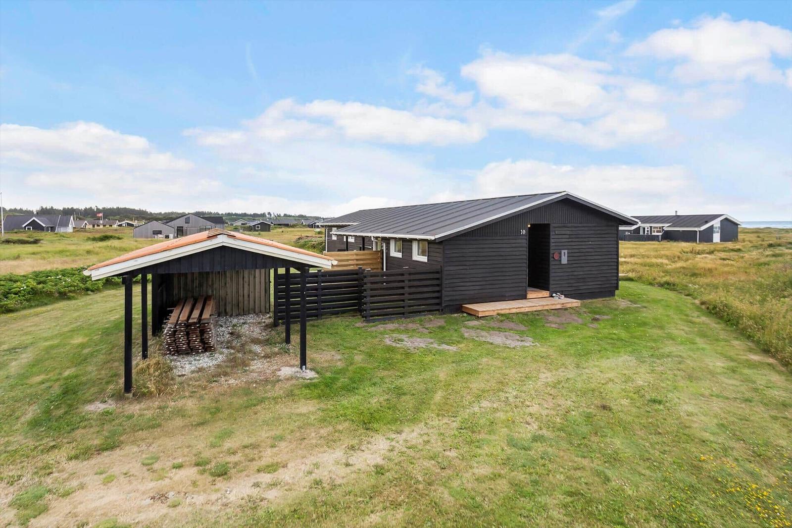 Schwarzes Holzhaus mit Holzveranda und Garten. Mehrere Häuser im Hintergrund.