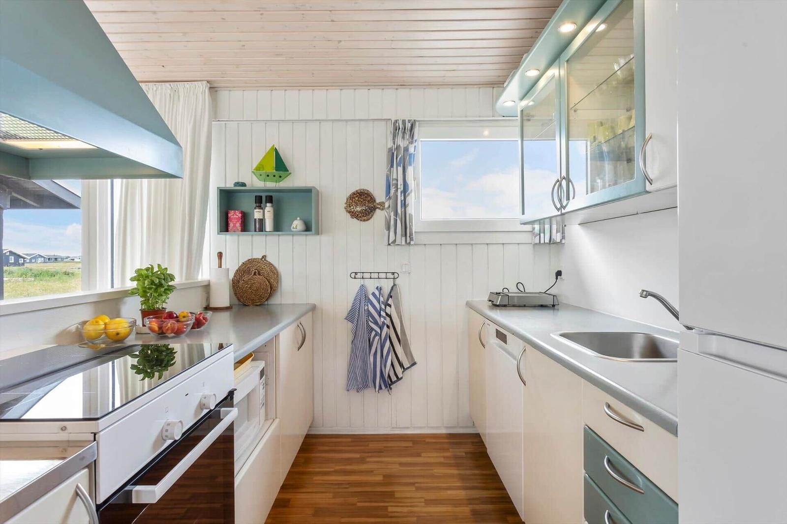 Küche mit weißen Schränken, Edelstahlspüle und Holzboden. Fenster mit Blick auf Grünfläche.