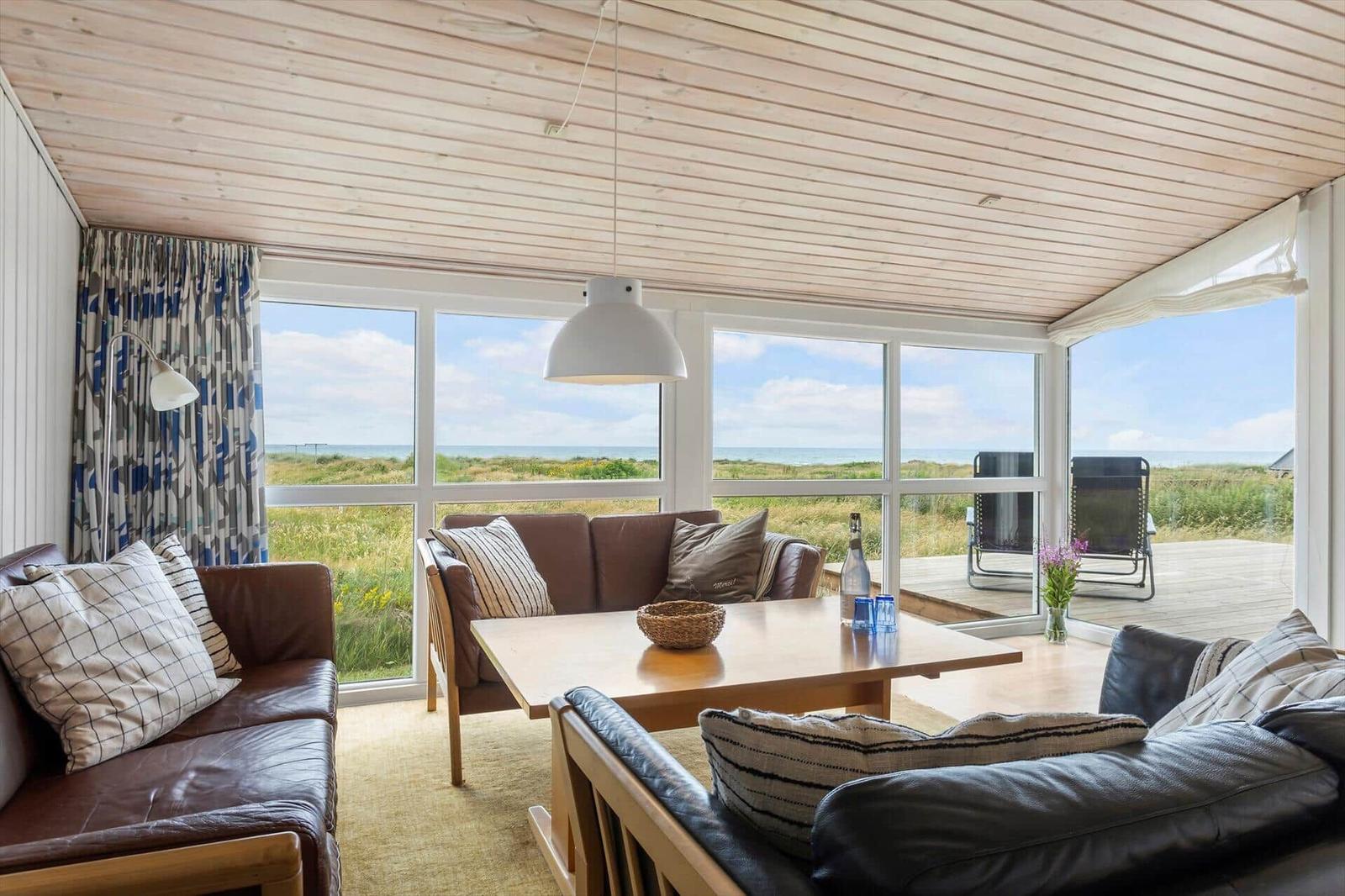 Wohnzimmer mit Blick auf Strand und Meer durch große Fenster.