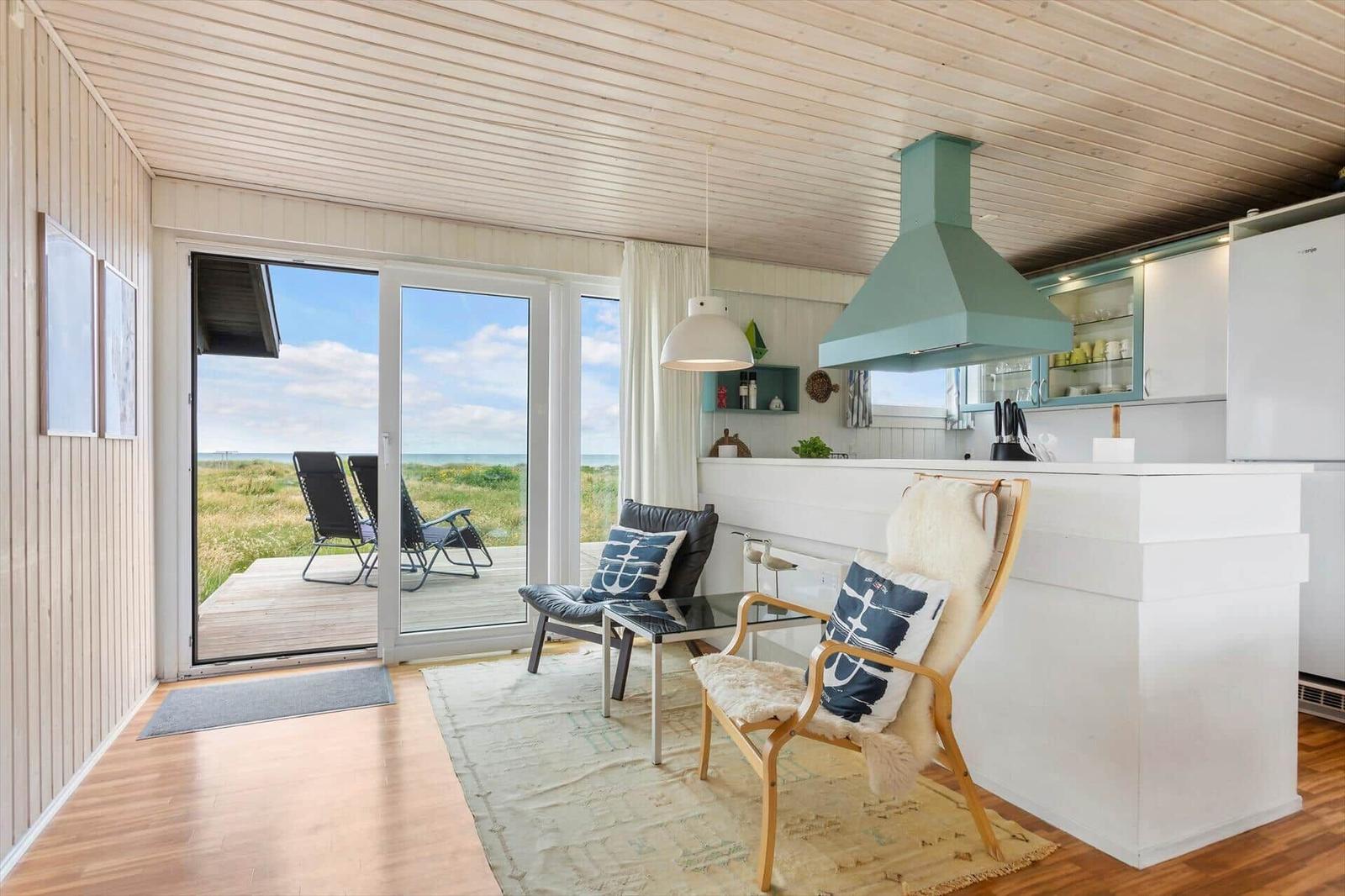 Küche mit Blick auf Terrasse und Strand. Holzdecke, weiße Arbeitsfläche und Sitzgelegenheiten.