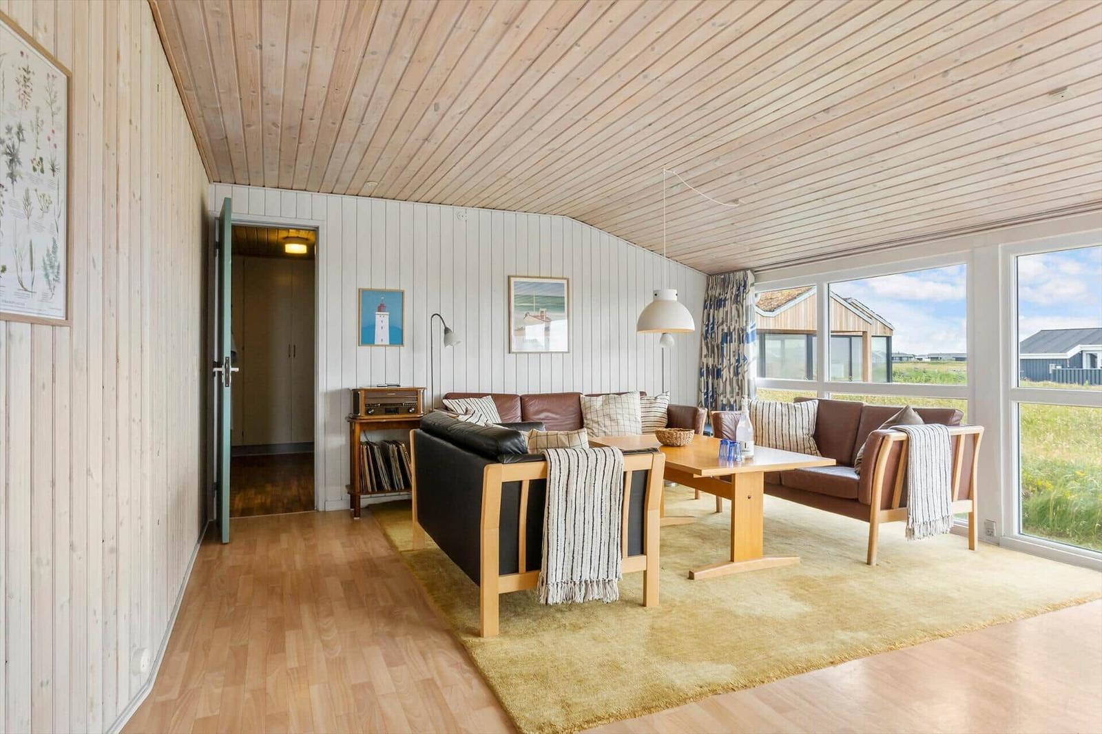 Wohnzimmer mit Holzboden, Sofa, Tisch und großen Fenstern.