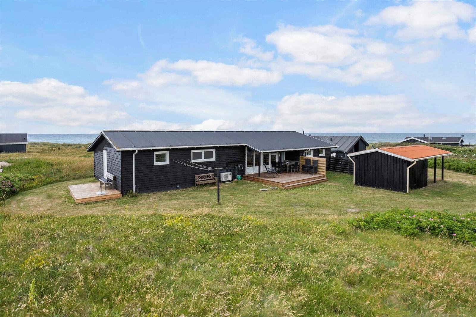 Schwarzes Ferienhaus mit Terrasse und Garten, Blick auf das Meer.