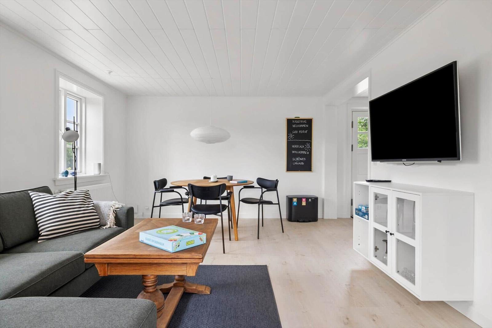 Wohn- und Essbereich mit Sofa, Tisch, Stühlen und Fernseher an der Wand.