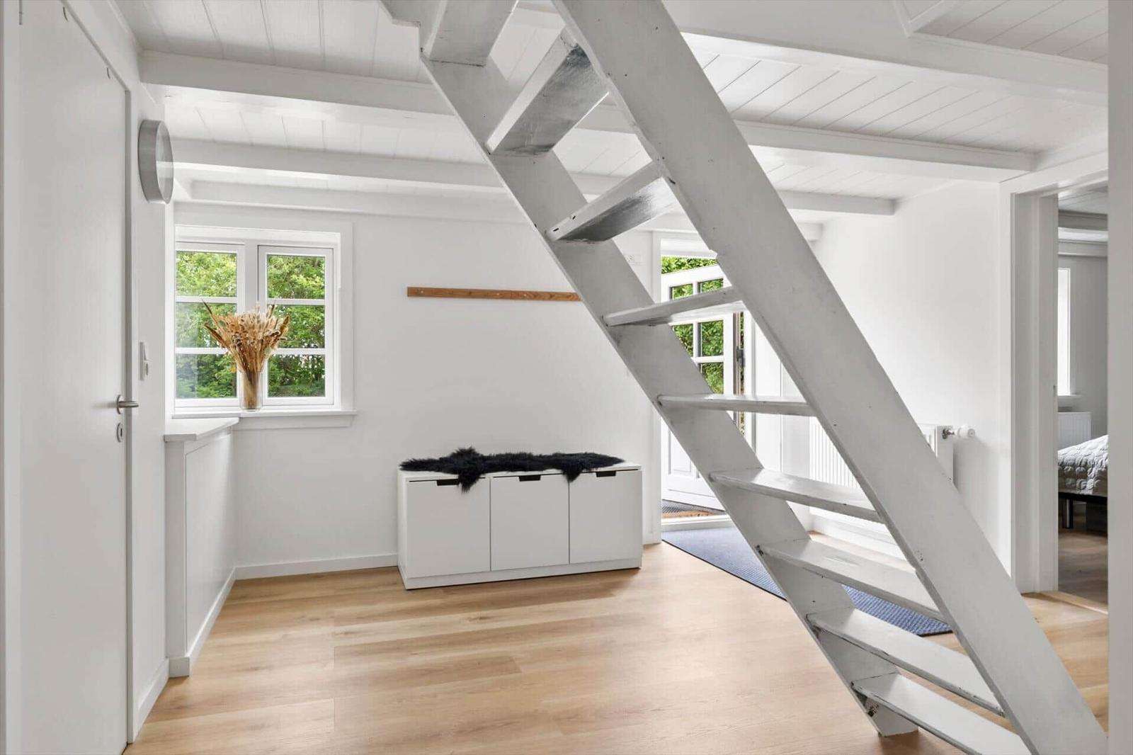 Raum mit Holzboden, weißer Treppe und Fenster mit Blick auf Grün.
