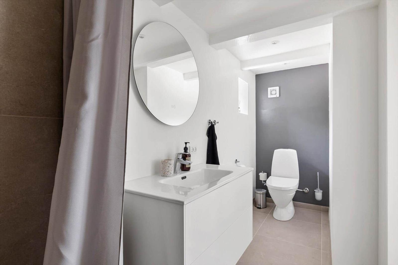 Badezimmer mit Waschbecken, Spiegel und Toilette. Dusche mit Vorhang.