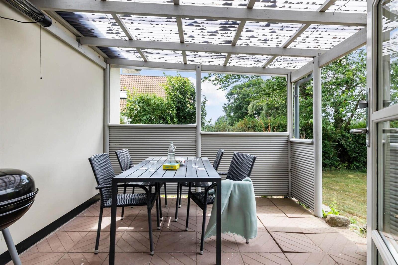 Terrasse mit Tisch, Stühlen und Grill unter Dach