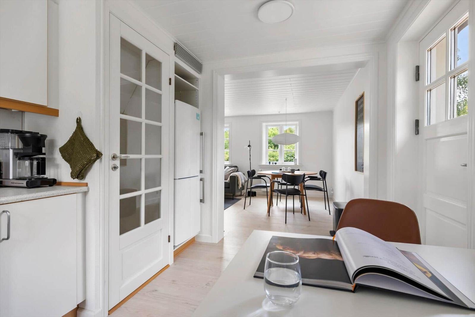 Küche mit Essbereich und Wohnzimmer im Hintergrund. Weiße Wände und Holzböden.