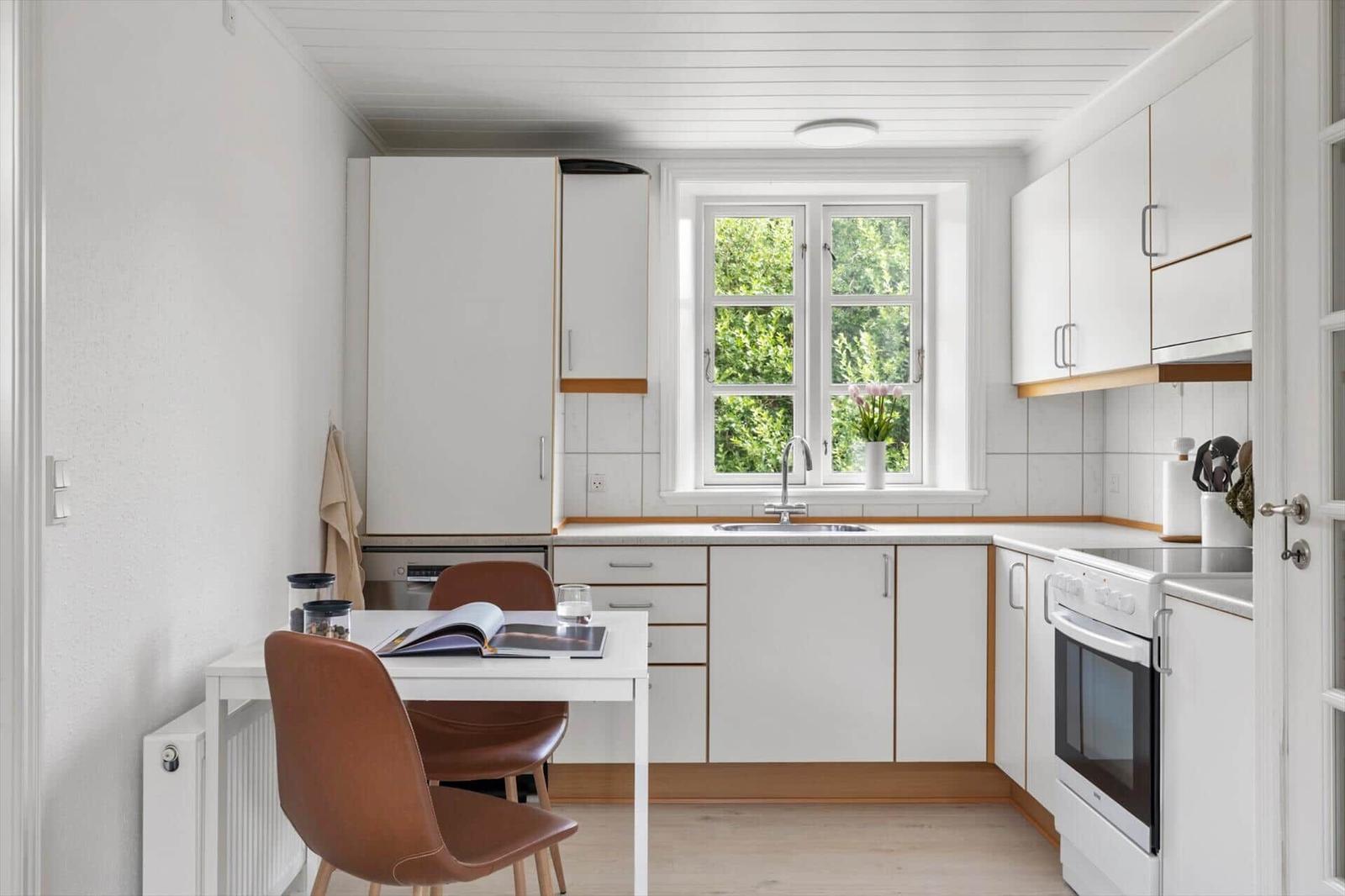 Küche mit weißer Einbauküche, Essplatz und Fenster mit Blick auf Grün.