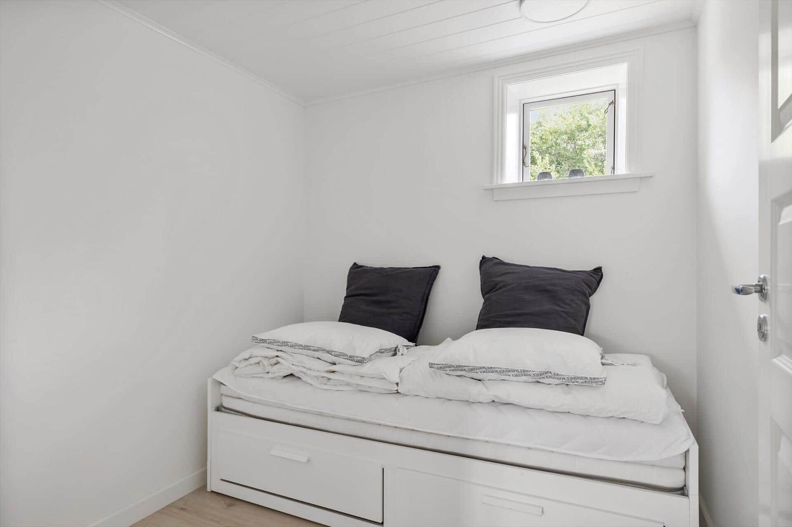 Schlafzimmer mit weißem Bett, zwei Kissen und kleinem Fenster.