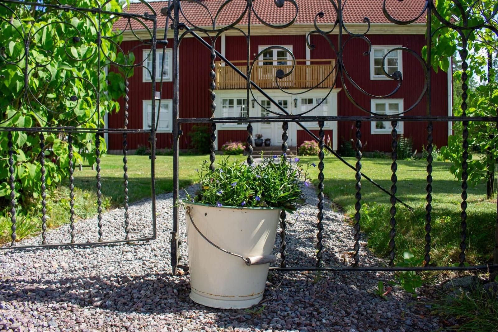 Roter Holzhaus mit Balkon hinter schmiedeeisernem Tor und Pflanzenkasten