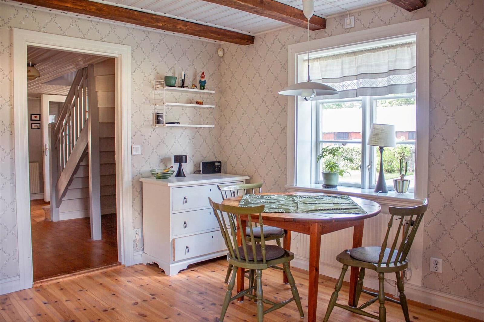 Esszimmer mit Holztisch, Stühlen und Fenster. Treppenhaus im Hintergrund.