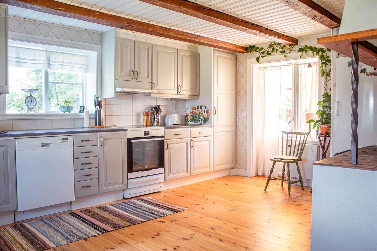 Küche mit Holzboden, weißen Schränken und Holzbalken an der Decke.