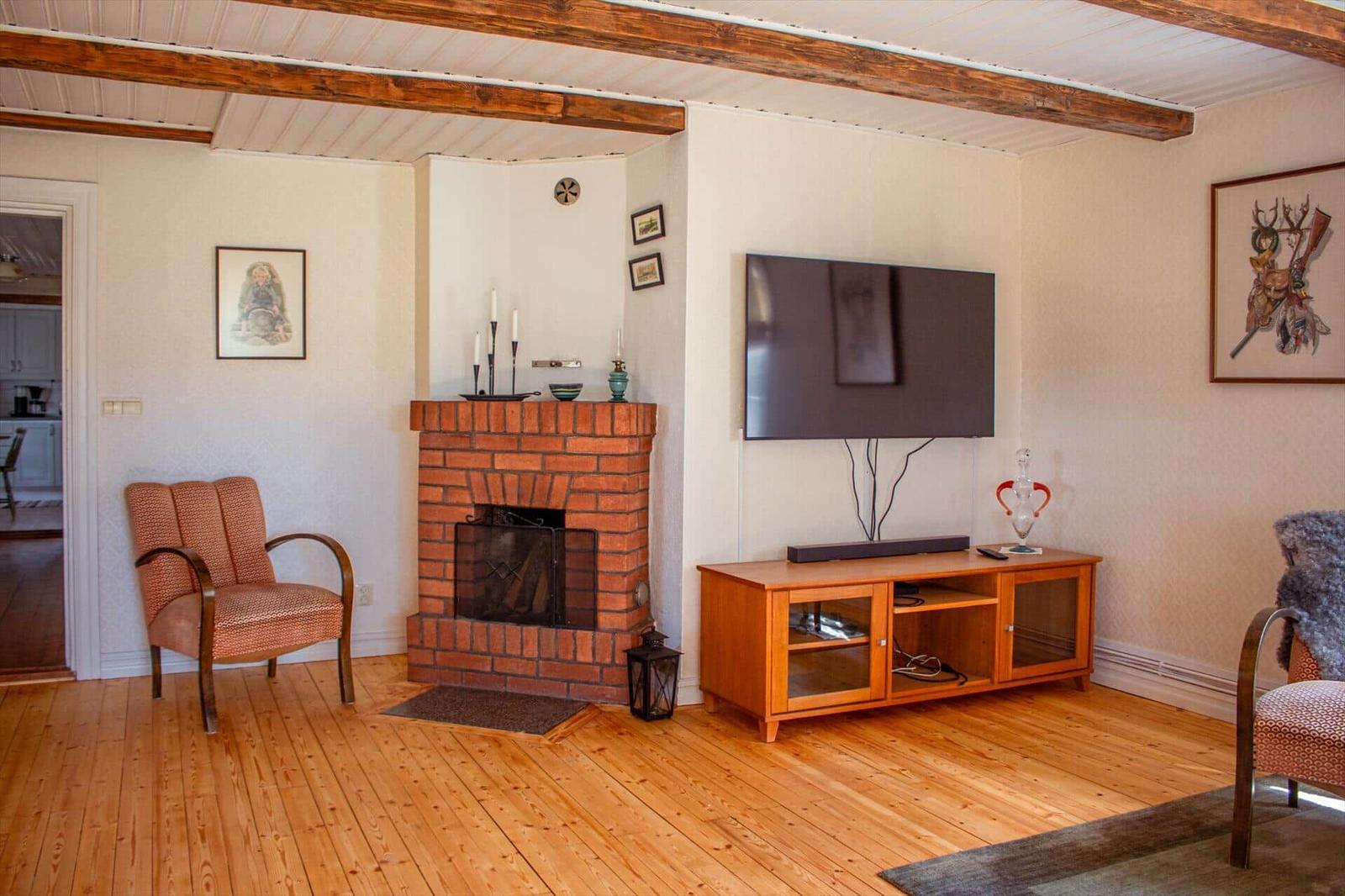 Wohnzimmer mit Kamin, Fernseher und Holzboden. Möbel und Bilder sorgen für gemütliche Atmosphäre.