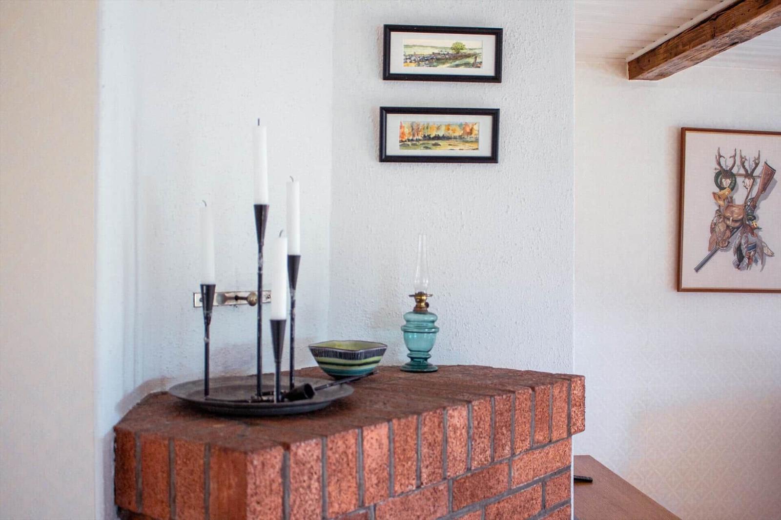 Kamin mit Kerzenhalter, Öllampe und Schale. Wandbilder und Holzbalken sichtbar.