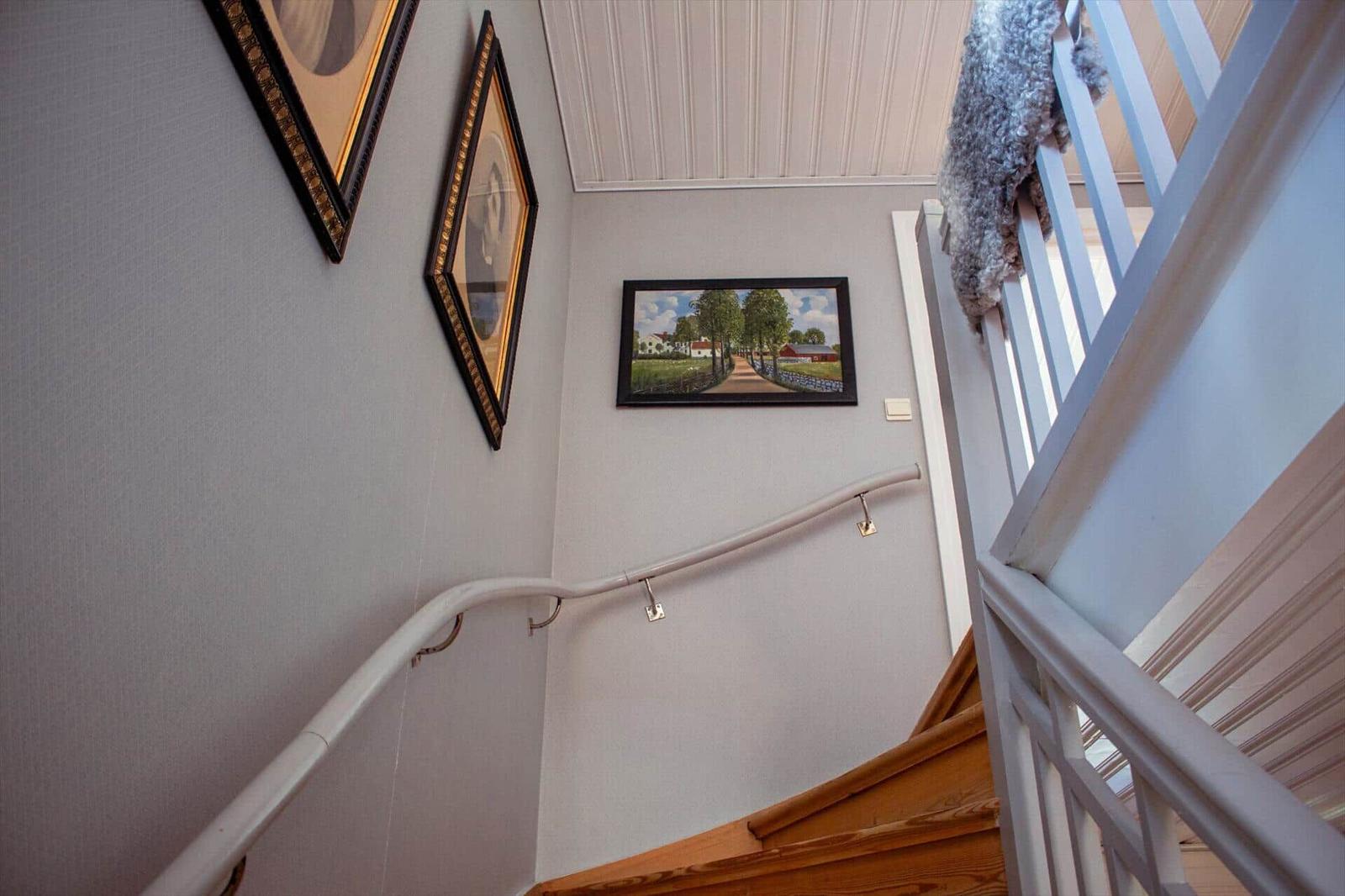 Hausflur mit Treppe, Wandbildern und weißen Geländern.