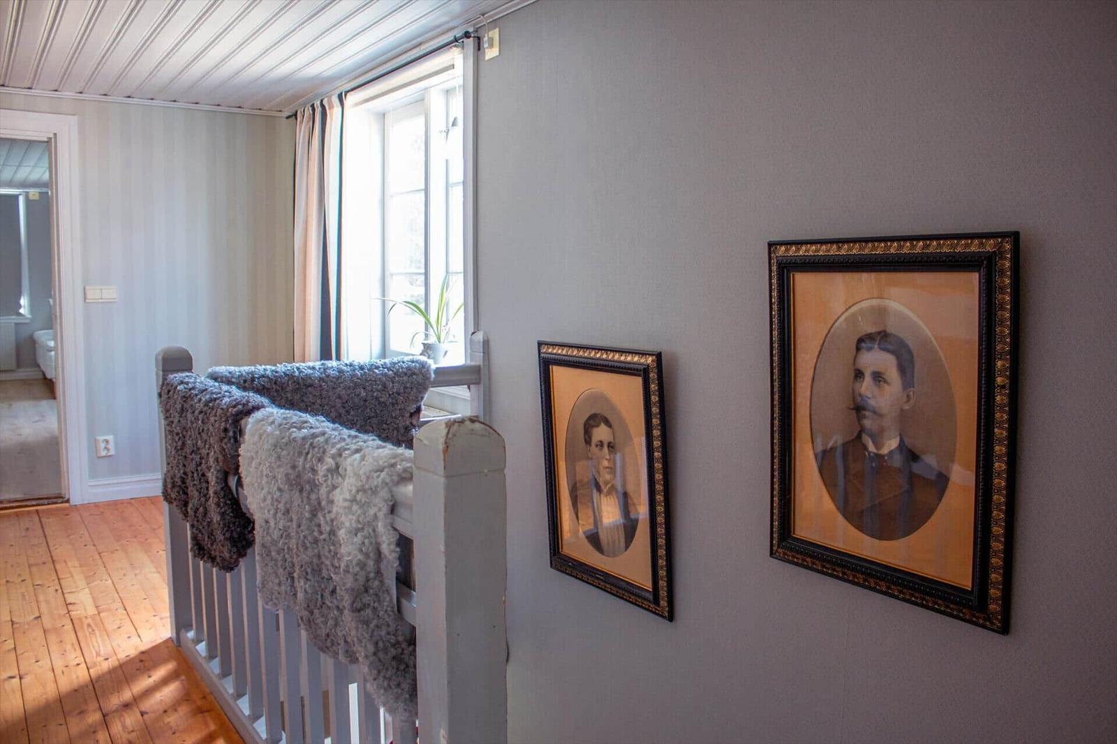 Wohnbereich mit Holzboden, Fenster und zwei gerahmten Porträts an der Wand.
