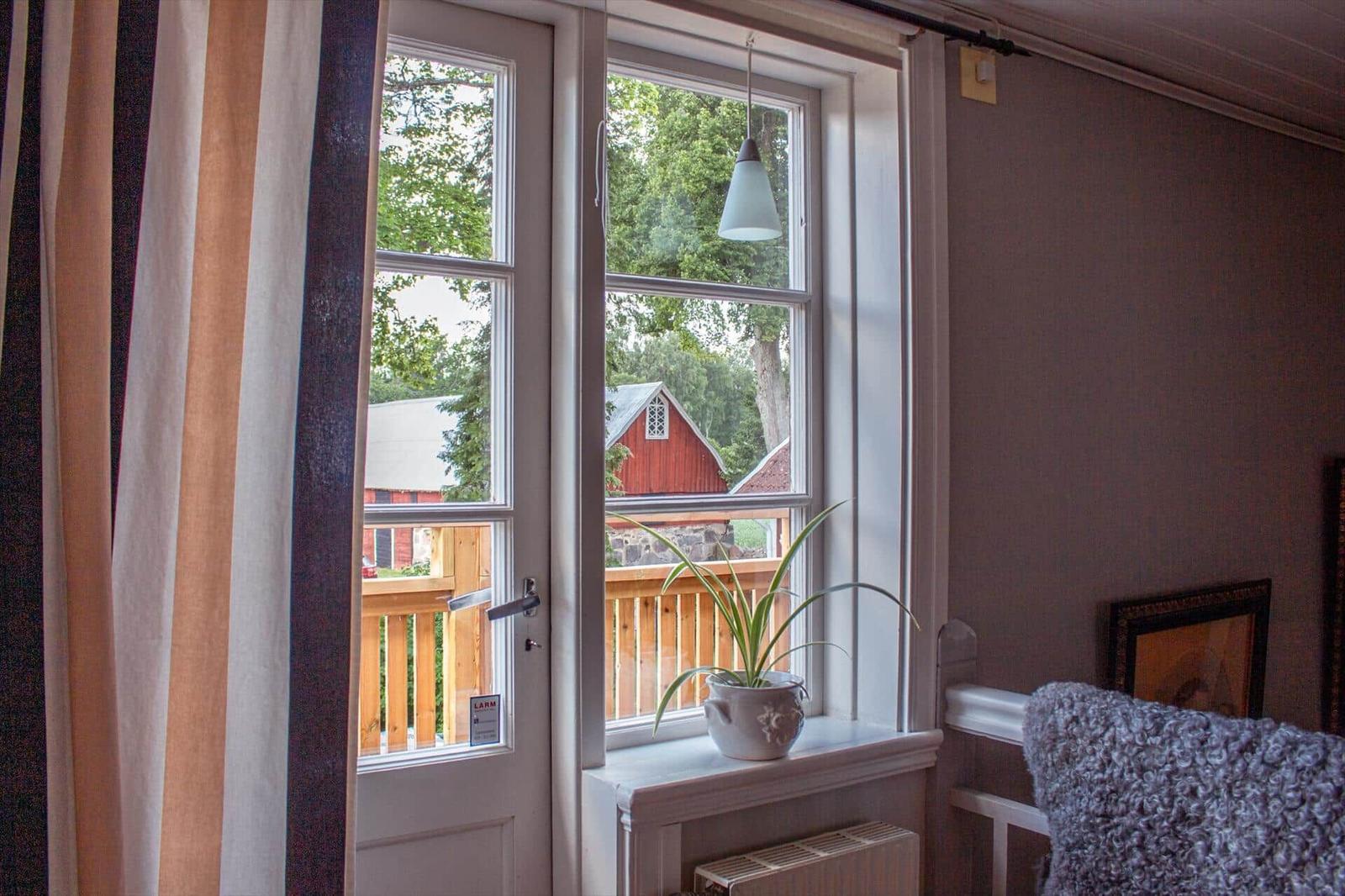 Durch das Fenster blickt man auf eine Holzterrasse und ein rotes Gebäude.