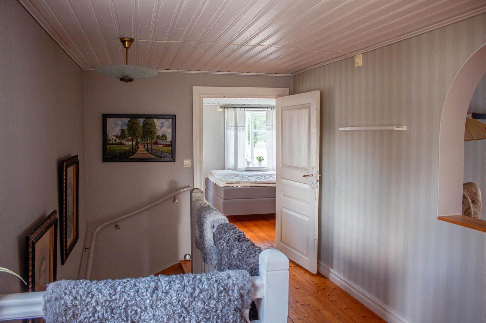 Hausflur mit Treppenhaus, Bildern an der Wand und Blick in Schlafzimmer mit Bett.
