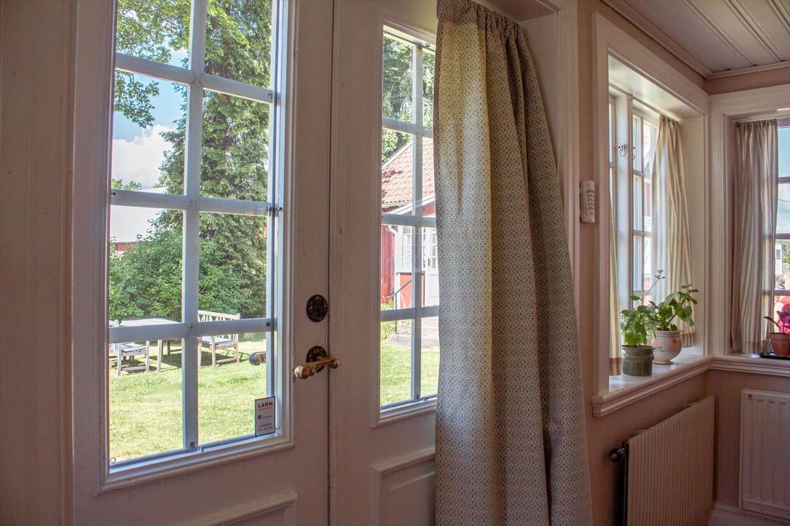 Helle Eingangshalle mit Fenstern, Vorhängen und Blick auf Garten.