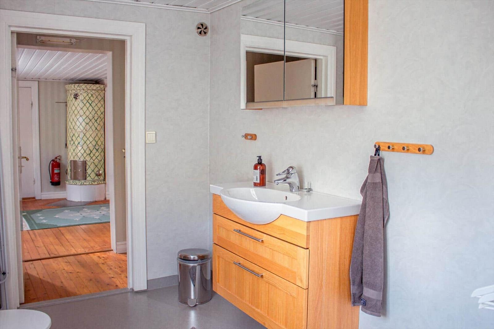 Bad mit Waschbecken, Spiegel und Handtuchhalter. Durchgang zu einem Raum mit Kamin.