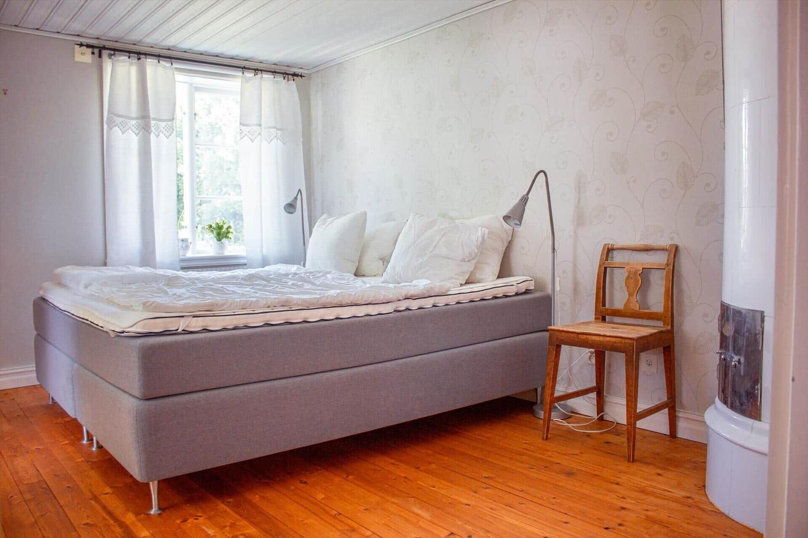 Schlafzimmer mit Bett, Stuhl und Fenster. Holzfußboden und Wand mit Muster.
