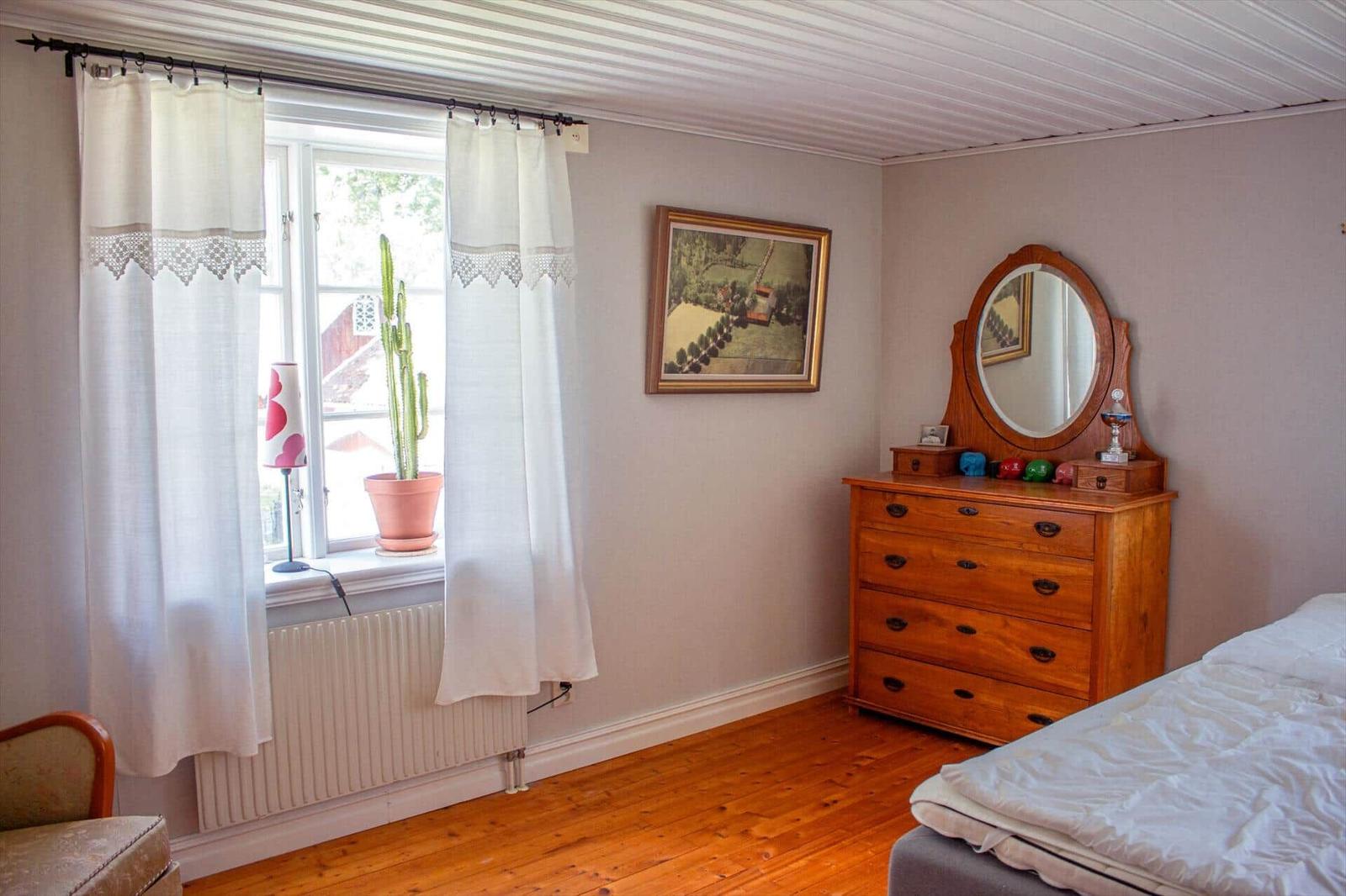 Schlafzimmer mit Holzboden, Bett, Schrank und Fenster mit Vorhängen.