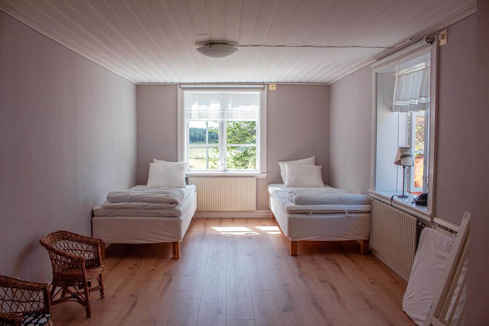 Zwei Betten, Fenster mit Blick, Holzboden, Stuhl und Lampe.