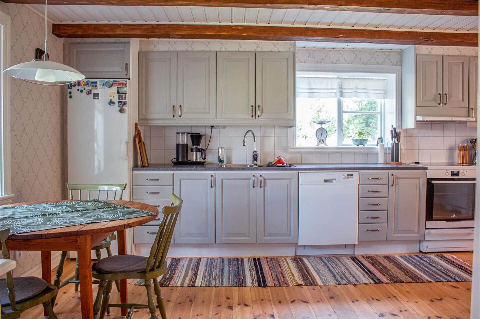 Küche mit Holzboden, hellen Schränken und Essbereich mit Tisch und Stühlen.