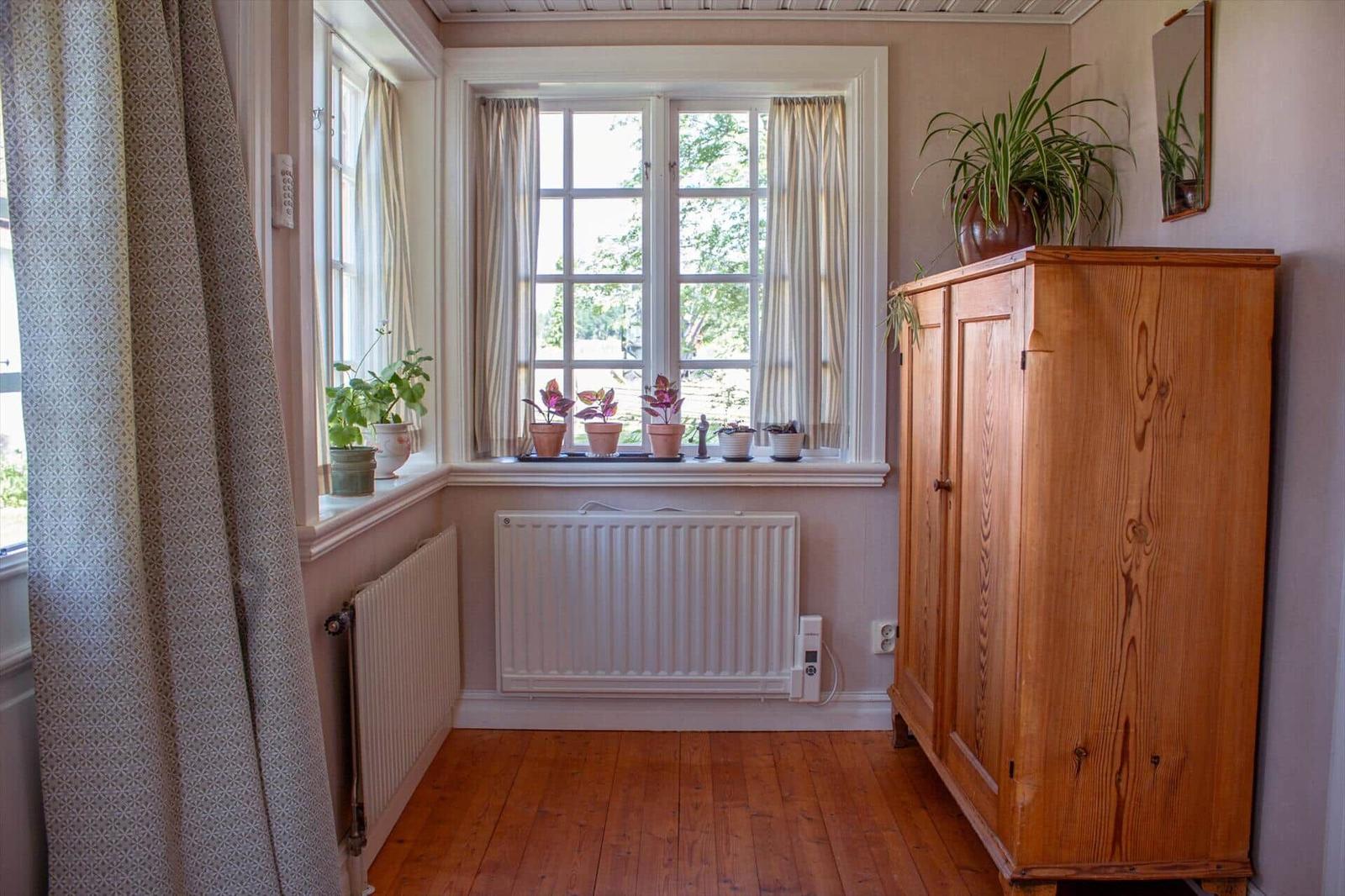 Raum mit Holzboden, Fenster, Pflanzen und Holzschrank.