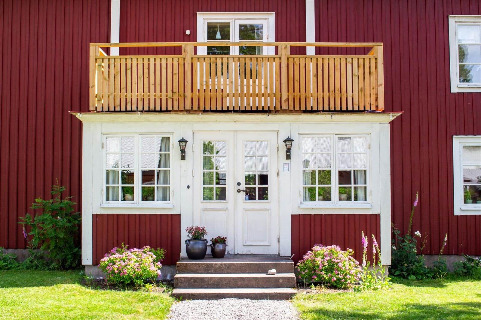 Rotes Holzhaus mit weißer Eingangstür, Balkon und Blumenbeeten.
