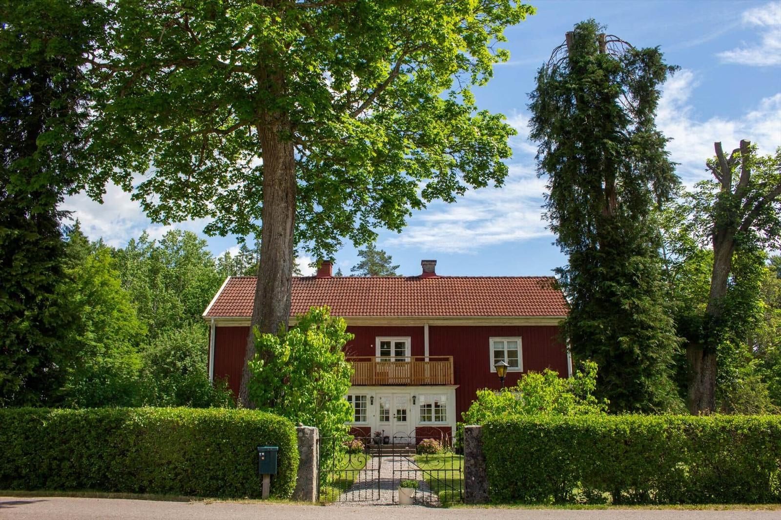 Rotes Haus mit Balkon, umgeben von Bäumen und Hecken.