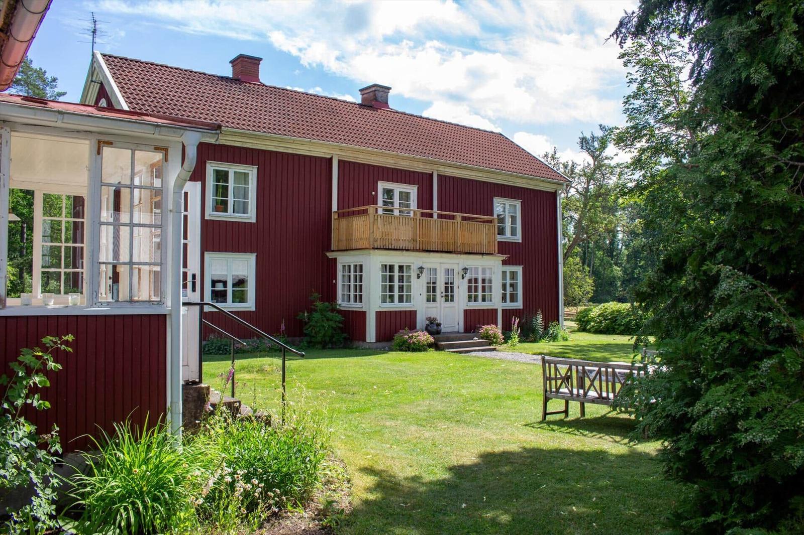Rotes Holzhaus mit Balkon, weißen Fenstern und grünem Garten.
