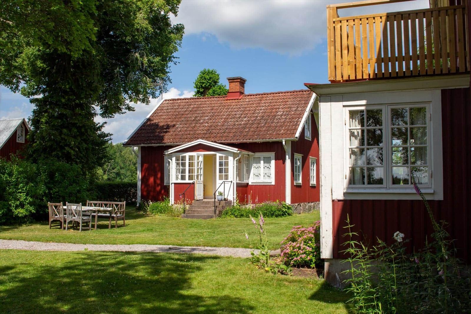 Rotes Haus mit Terrasse, Garten und Tisch. Helle Fenster, roter Dachfirst.