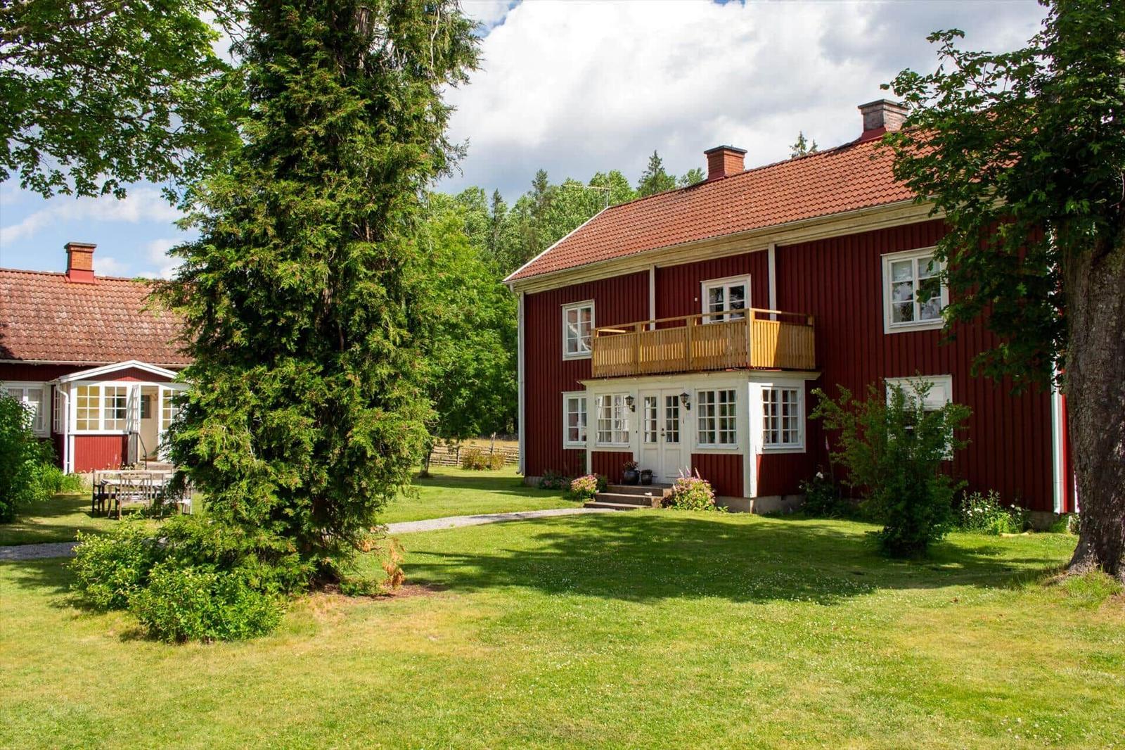 Rotes Holzhaus mit Balkon und grünem Garten. Hinterhof mit Tisch und Stühlen.