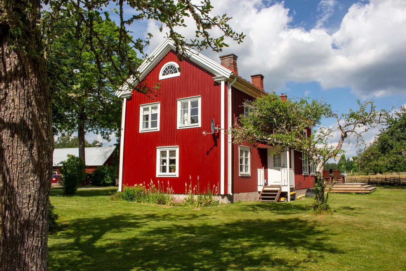 Rotes Holzhaus mit weißen Fensterrahmen und Garten. Hinterhof mit Holzterrasse und Bäumen.