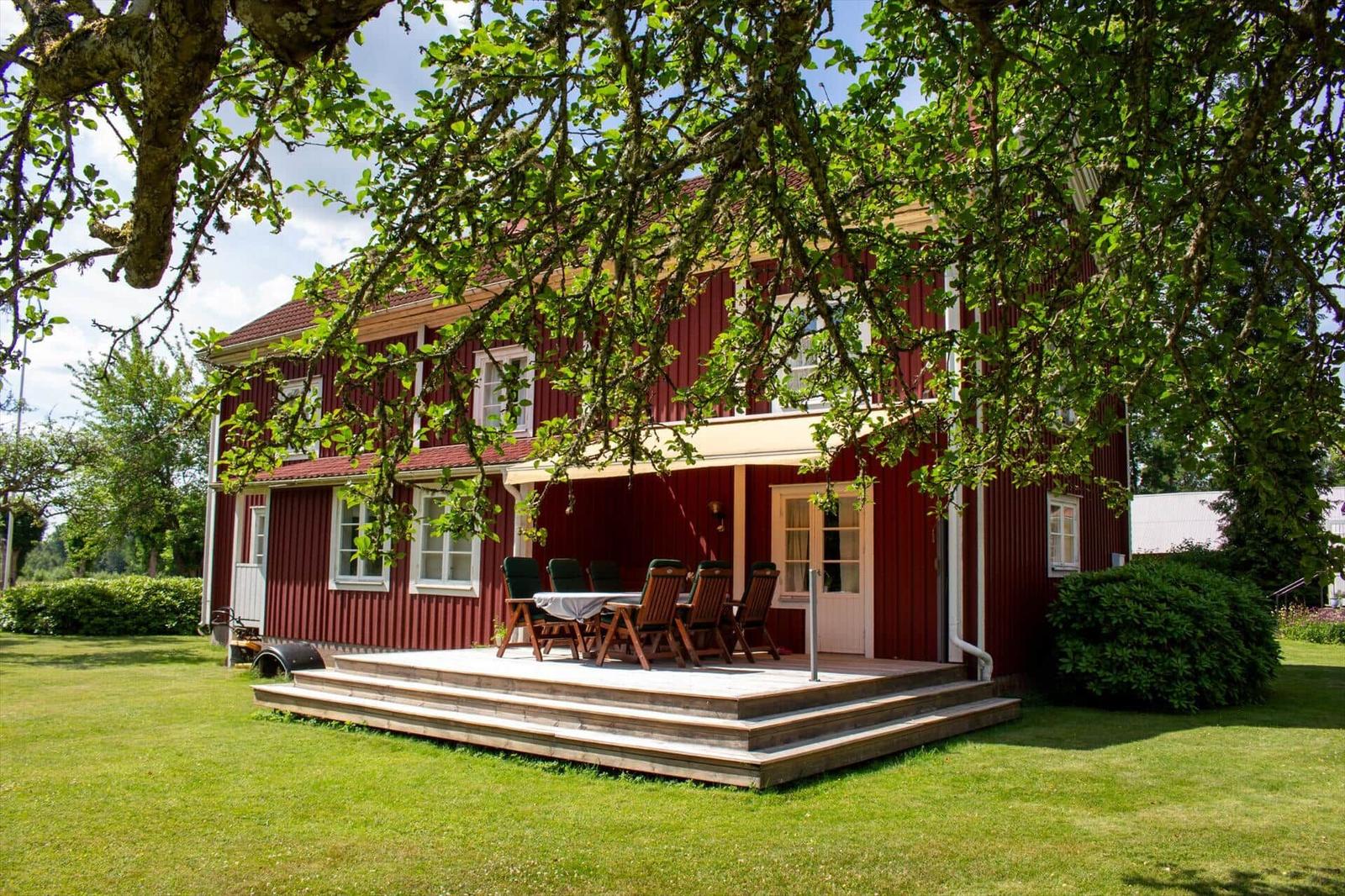 Rotes Holzhaus mit Terrasse und Garten. Tisch und Stühle auf der Veranda.